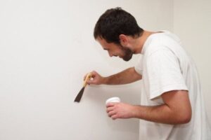 Painter inspecting, repairing, and sanding interior walls to prepare the surface before applying paint