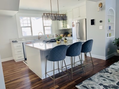 White painted kitchen cabinets with navy blue bar stools and hardwood flooring