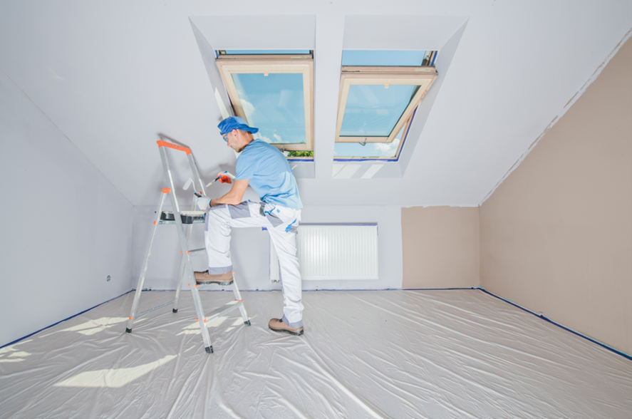 Man on ladder in empty room, showcasing interior commercial painters at work.